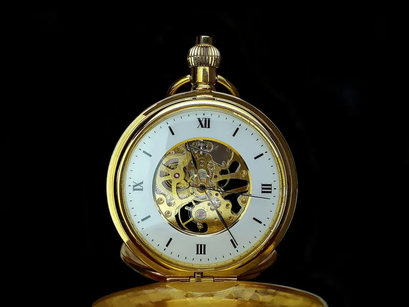 Detailed close-up of a vintage gold mechanical pocket watch on a black background, showcasing gears and roman numerals.